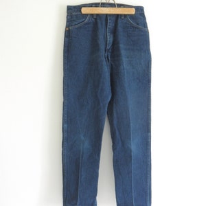 May include: A pair of dark blue denim jeans hanging on a wooden hanger. The jeans have a straight leg and a classic five-pocket design.