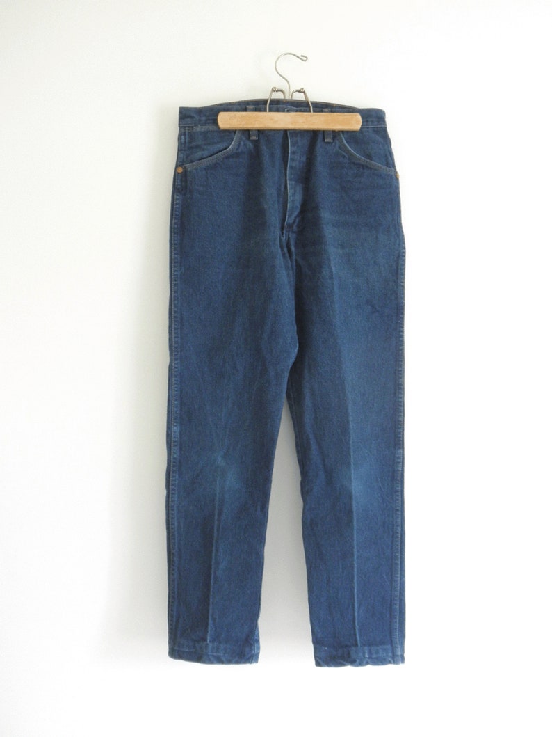 May include: A pair of dark blue denim jeans hanging on a wooden hanger. The jeans have a straight leg and a classic five-pocket design.