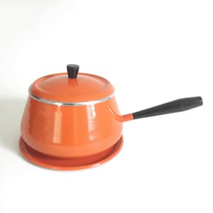 May include: Orange enamel fondue pot with a black handle and a matching orange base. The pot has a lid with a black knob.