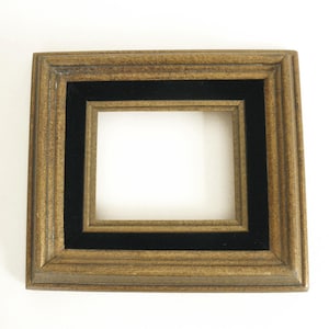 May include: A rectangular picture frame with a gold-toned, textured border and a black velvet inner border. The frame has a recessed area for a photo or artwork. The frame is empty.