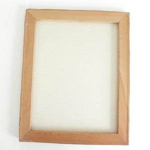 May include: A rectangular wooden frame with mitered corners holding a blank, off-white canvas. The frame is constructed from light-colored, natural wood with a visible grain pattern, providing a sturdy border for the stretched fabric surface.
