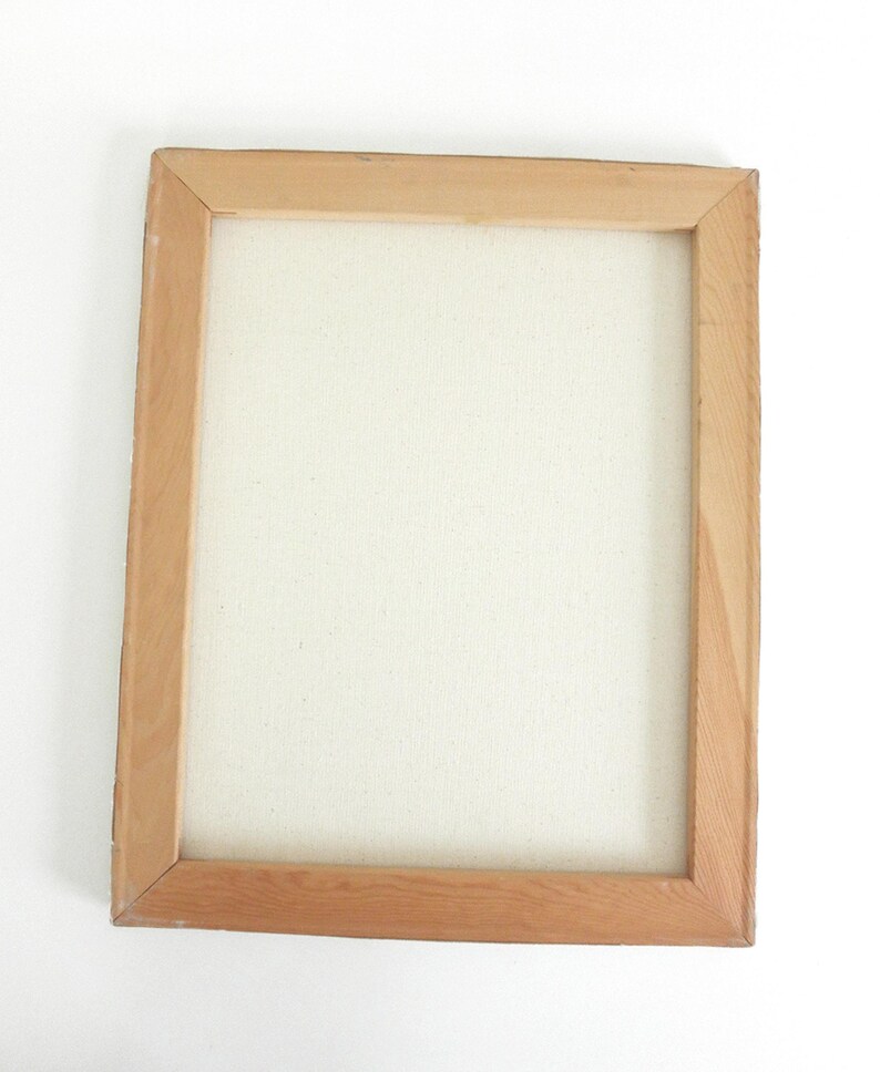 May include: A rectangular wooden frame with mitered corners holding a blank, off-white canvas. The frame is constructed from light-colored, natural wood with a visible grain pattern, providing a sturdy border for the stretched fabric surface.