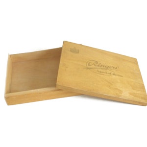 May include: A wooden box with a hinged lid. The lid has the text "Ringers' Specialiteter" printed on it.
