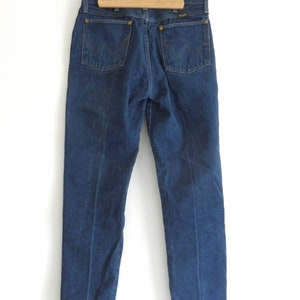 May include: A pair of dark blue denim jeans with a classic straight leg fit. The jeans have a leather patch on the back with the Wrangler logo.