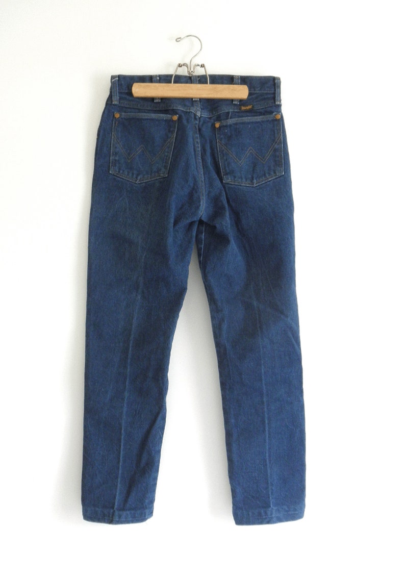 May include: A pair of dark blue denim jeans with a classic straight leg fit. The jeans have a leather patch on the back with the Wrangler logo.