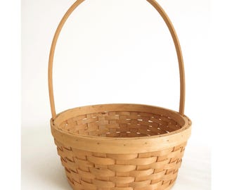 May include: A natural woven basket with a round base and a single wooden handle.