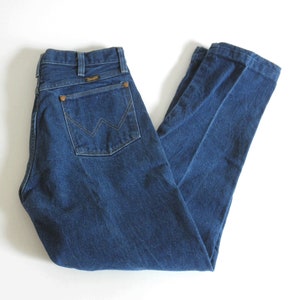 May include: A pair of dark blue denim jeans with a brown leather patch on the back pocket that says "Wrangler".
