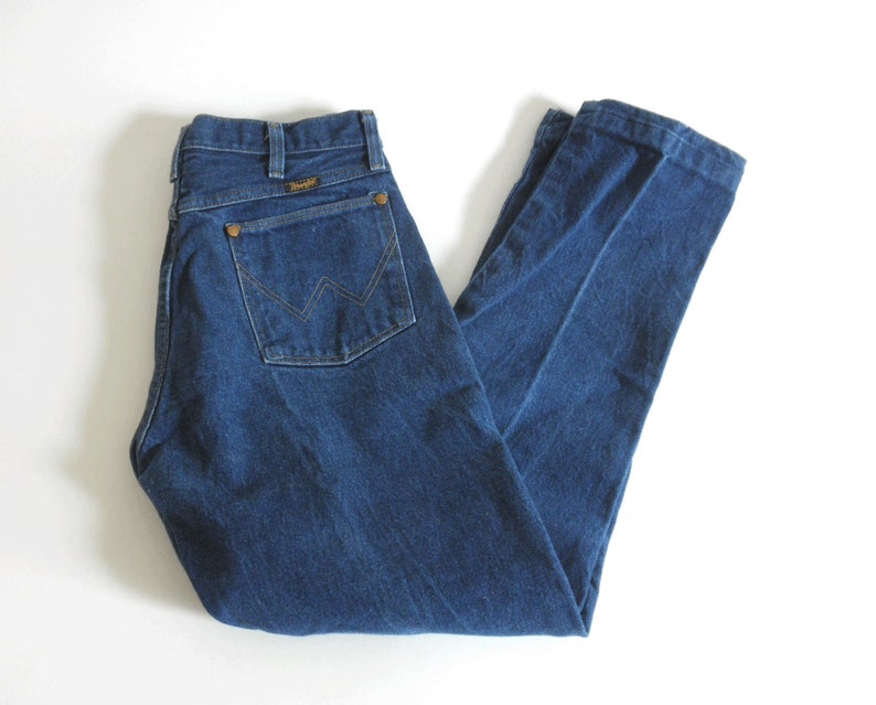 May include: A pair of dark blue denim jeans with a brown leather patch on the back pocket that says "Wrangler".