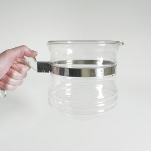 May include: A clear glass coffee pot with a metal band around the middle and a plastic handle.