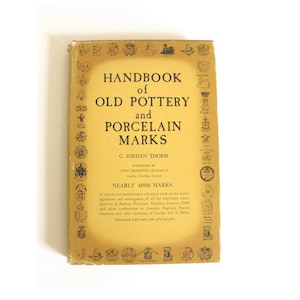 May include: A yellow book titled "Handbook of Old Pottery and Porcelain Marks" by C. Jordan Thorn. The book cover features a border of black and white illustrations of pottery and porcelain marks. The book includes a foreword by John Meredith Graham II.
