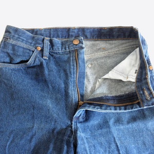 May include: A pair of blue denim jeans with a zip fly and a button fastening. The jeans are undone and the zip is partially open.