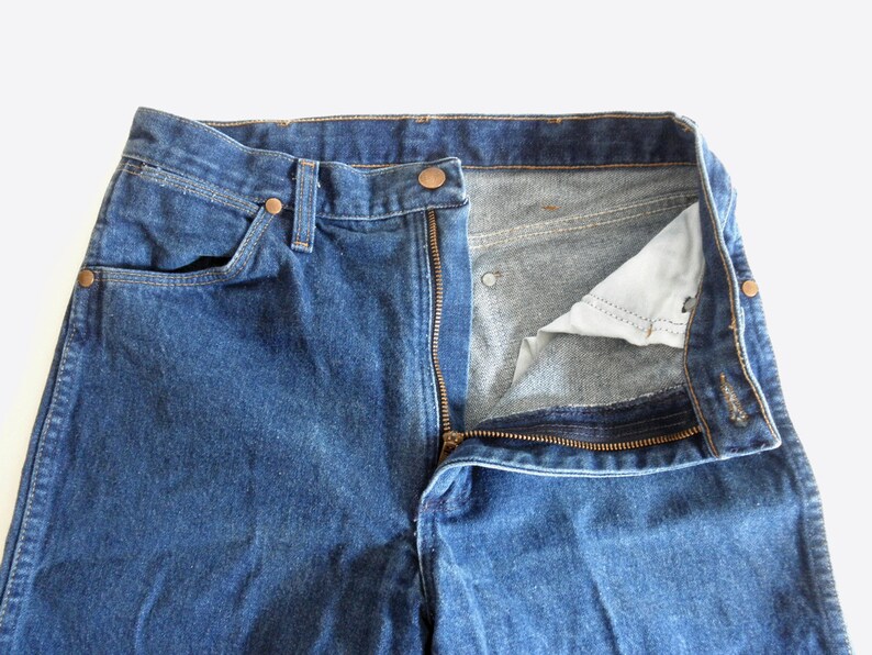May include: A pair of blue denim jeans with a zip fly and a button fastening. The jeans are undone and the zip is partially open.