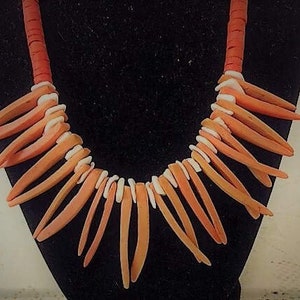 May include: A necklace made of orange and white coral pieces. The coral pieces are shaped like long, thin spikes. The necklace is on a black background.