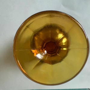 May include: A top-down view of a vintage amber-colored glass. The glass has a wide, shallow bowl and a short stem. The glass is made of a transparent material, and the light reflects off the surface, creating a warm, inviting glow.