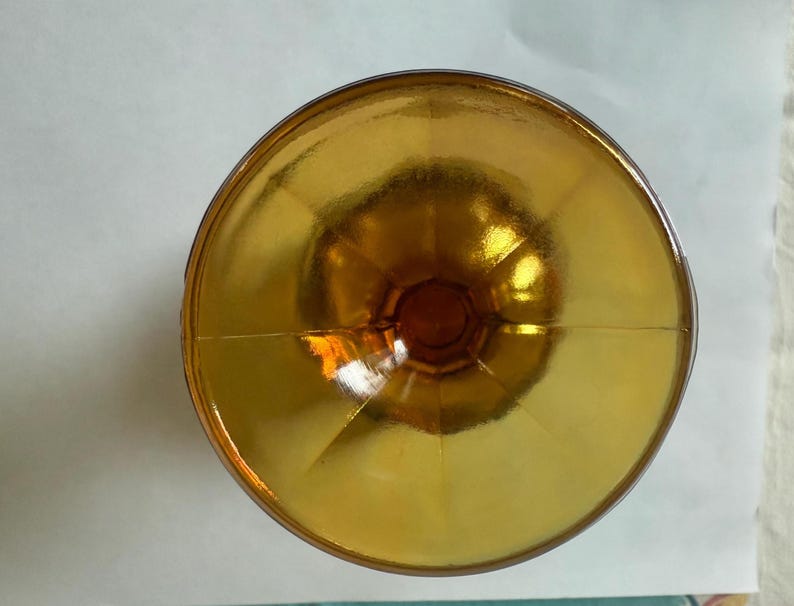 May include: A top-down view of a vintage amber-colored glass. The glass has a wide, shallow bowl and a short stem. The glass is made of a transparent material, and the light reflects off the surface, creating a warm, inviting glow.