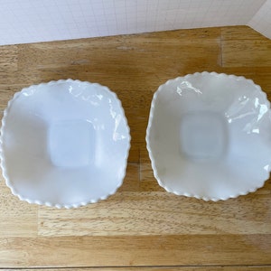 May include: Two white ceramic bowls with scalloped edges. The bowls are square shaped and have a smooth, glossy finish.