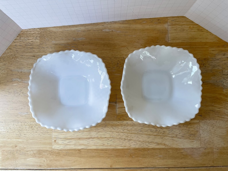 May include: Two white ceramic bowls with scalloped edges. The bowls are square shaped and have a smooth, glossy finish.