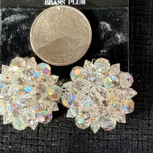 Puede incluir: Un par de pendientes vintage de racimo de cristal transparente. Cada pendiente presenta un dise&ntilde;o floral con m&uacute;ltiples facetas, que refleja colores iridiscentes. Se incluye una moneda de 25 centavos de d&oacute;lar estadounidense como referencia de tama&ntilde;o.