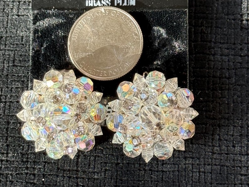 Puede incluir: Un par de pendientes vintage de racimo de cristal transparente. Cada pendiente presenta un dise&ntilde;o floral con m&uacute;ltiples facetas, que refleja colores iridiscentes. Se incluye una moneda de 25 centavos de d&oacute;lar estadounidense como referencia de tama&ntilde;o.