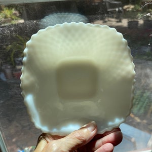May include: A white milk glass square dish with a scalloped edge. The dish has a textured surface and is slightly iridescent.