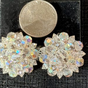 Puede incluir: Un par de pendientes de cristal transparente y brillante con un dise&ntilde;o floral. Cada pendiente presenta m&uacute;ltiples facetas que capturan la luz, creando un efecto deslumbrante. Una moneda est&aacute; al lado de los pendientes para la comparaci&oacute;n de tama&ntilde;o.