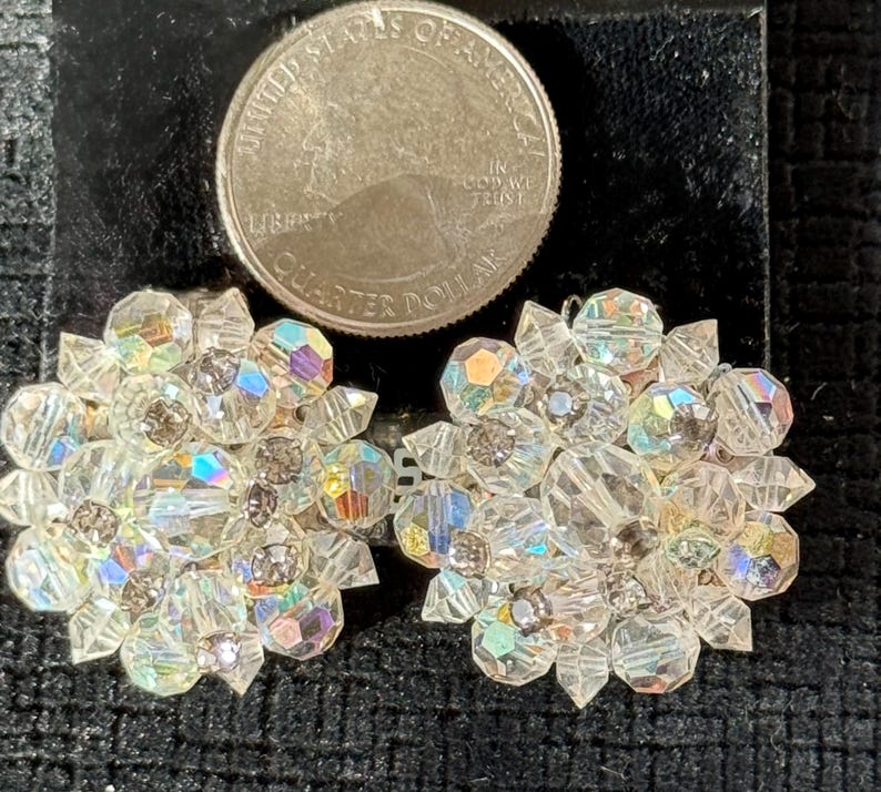Puede incluir: Un par de pendientes de cristal transparente y brillante con un dise&ntilde;o floral. Cada pendiente presenta m&uacute;ltiples facetas que capturan la luz, creando un efecto deslumbrante. Una moneda est&aacute; al lado de los pendientes para la comparaci&oacute;n de tama&ntilde;o.