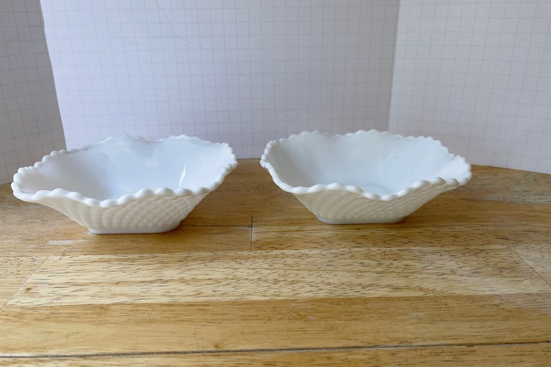 May include: Two white ceramic bowls with a scalloped edge and a textured design. The bowls are sitting on a wooden surface.