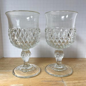 May include: Two clear, vintage-style wine glasses. The upper portion of the glasses is smooth, while the lower half features a diamond-cut pattern. Each glass has a stem and a round base, perfect for serving wine or other beverages.