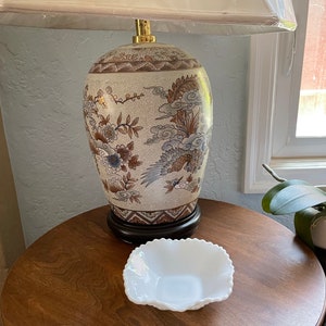 May include: A white ceramic lamp base with a brown and gold floral design. The lamp is on a wooden table with a white ceramic bowl.