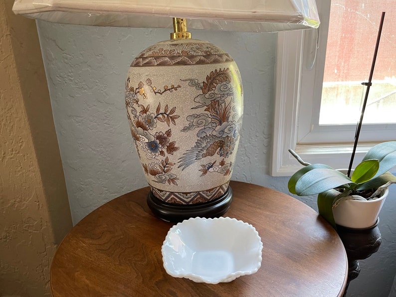 May include: A white ceramic lamp base with a brown and gold floral design. The lamp is on a wooden table with a white ceramic bowl.