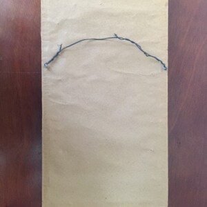 May include: The back of a framed picture with a brown paper backing and a black wire hanger attached.