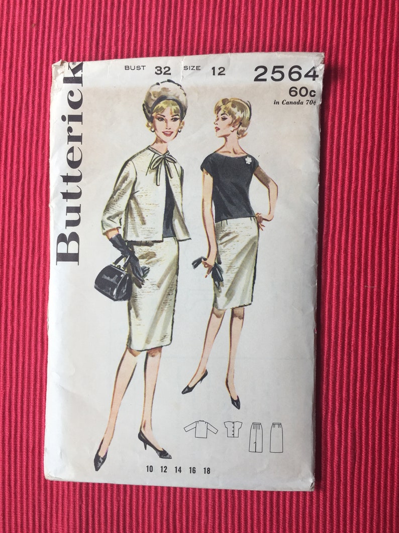 Pu&ograve; includere: Una busta per cartamodello Butterick, numero 2564, taglia 12, busto 32. L'illustrazione mostra due figure che indossano un completo gonna e giacca abbinato, con un top scuro, guanti neri e una borsa. Include disegni al tratto dei capi.