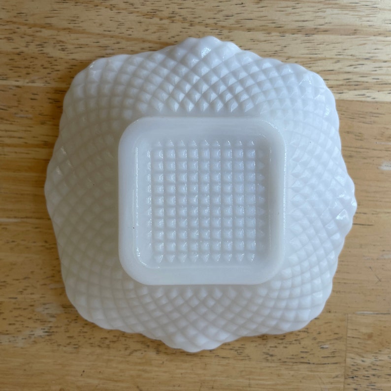 May include: White milk glass bowl with a square, raised, textured center. The bowl has a scalloped edge and a diamond pattern.
