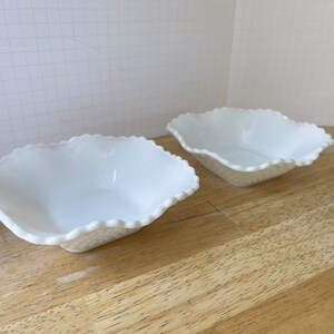 May include: Two white, scalloped, ceramic bowls on a wooden surface.