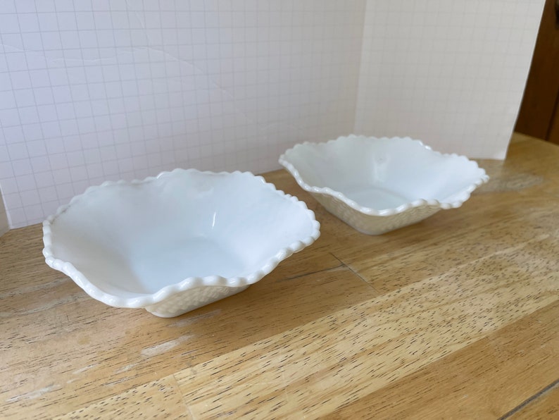 May include: Two white, scalloped, ceramic bowls on a wooden surface.