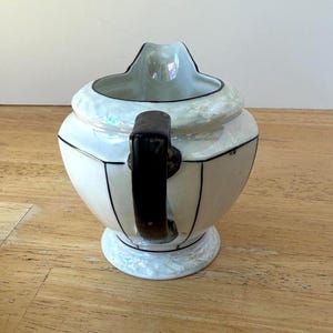 Puede incluir: Una cremera de cer&aacute;mica blanca y negra con un asa negra. La cremera tiene un acabado nacarado y un dise&ntilde;o geom&eacute;trico. La cremera est&aacute; sobre una peque&ntilde;a base de pedestal. La cremera es probablemente vintage.
