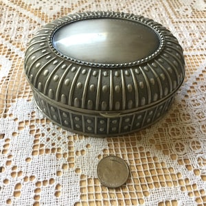 Vintage Jewelry Box. Oval casket with domed, hinged lid & black velvet lining. Embossed, patterned pewter that is silver colored. 5+" long.