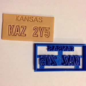 May include: A tan leather stamp with the word "KANSAS" and the letters "KAZ 2Y5" embossed on it. A blue plastic mold with the same text in reverse is also shown.