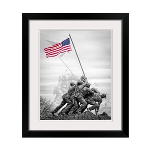 May include: Black and white photograph of the Iwo Jima Memorial, a statue of five Marines raising the American flag on Mount Suribachi during World War II. The statue is set against a cloudy sky with a waving American flag in the foreground.