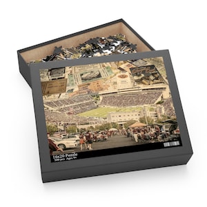 Puede incluir: Una caja de rompecabezas de 40,6 x 50,8 cm con un collage de un estadio de fútbol y boletos antiguos. La caja está abierta, revelando las piezas del rompecabezas. La caja dice "16x20 Puzzle 500 pcs Ages 9+". La imagen tiene un tono sepia.