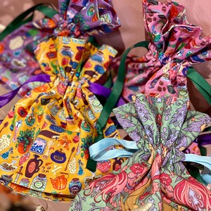 May include: A collection of colorful drawstring bags with various patterns. The bags feature designs with jars, teapots, and floral motifs. Each bag is tied with a contrasting ribbon, including green, purple, and blue.