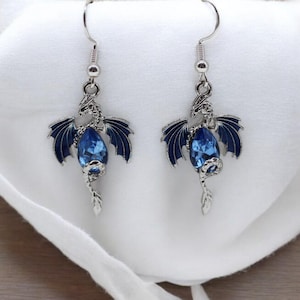 May include: A pair of silver dragon earrings with blue crystal accents. The dragons are detailed with wings and a tail.