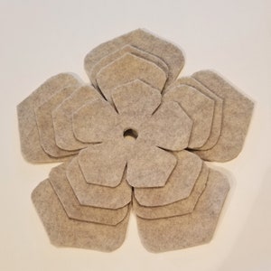May include: A beige felt flower with multiple layers of petals, creating a 3D effect. The flower has a small hole in the center.