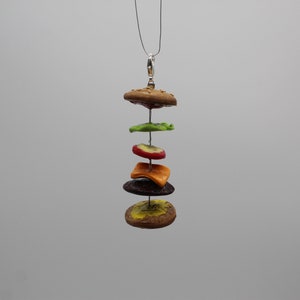 May include: A silver chain necklace with a polymer clay hamburger pendant. The pendant is made up of a bun, lettuce, tomato, cheese, a patty, and another bun.