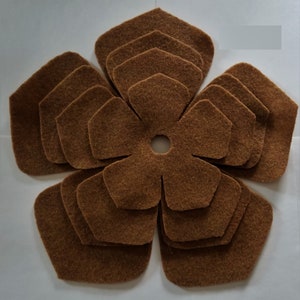 May include: A brown felt flower with multiple layers of petals. The flower has a central hole in the middle.