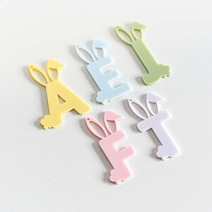 May include: Five pastel colored acrylic letters with bunny ears. The letters spell out the word "A E F T".