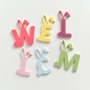 May include: A set of six pastel-colored letters spelling out "WELCOME" with bunny ears on top. The letters are made of a thick, plastic material and are perfect for decorating a home or classroom.