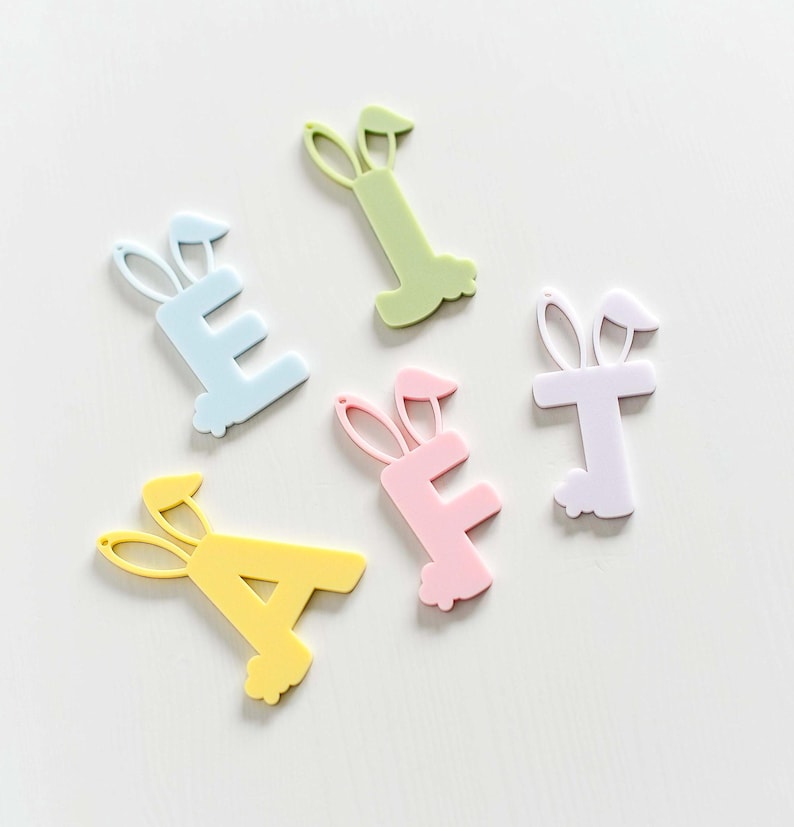May include: Five pastel colored letters, A, E, F, T, and I, with bunny ears, are arranged on a white surface. The letters are made of plastic and are in various pastel colors, including yellow, blue, pink, purple, and green.