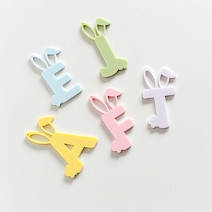May include: Five pastel colored plastic letters, A, E, E, T, and I, each with bunny ears, on a white background.