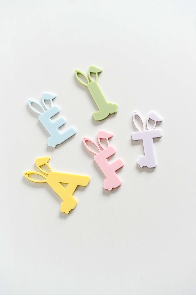 May include: Five pastel colored plastic letters, A, E, E, T, and I, each with bunny ears, on a white background.